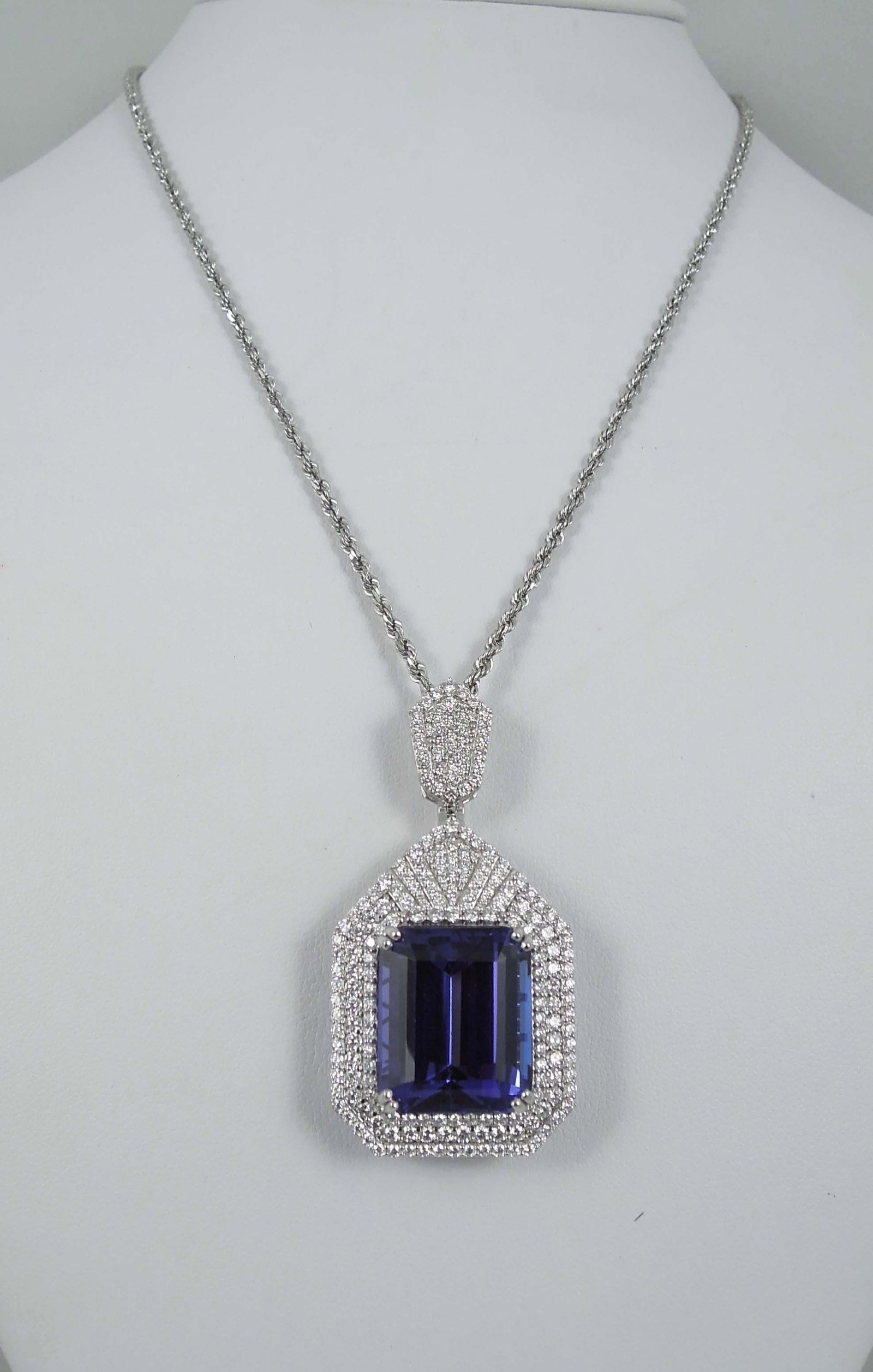 FINE LADIES PLATINUM, TANZANITE & DIAMOND NECKLACE: An 18K rope chain supports a large diamomd encrusted pendant set with a center octagonal stem cut tanzanite with excellent bluish violet coloration. Tanzanite weighs 28.25 cts. and is accompanied by a