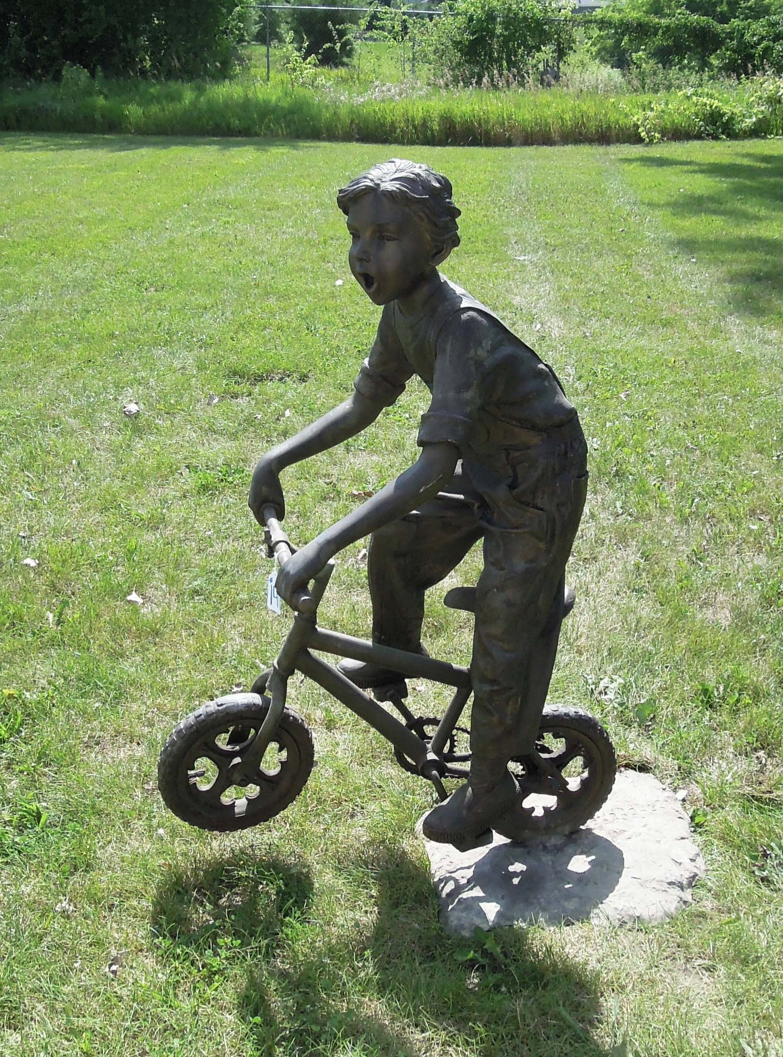 VINTAGE LIFE SIZE BRONZE SCULPTURE OF YOUNG BOY RIDING BICYCLE: Great aged patina. Very heavy. Front wheel spins. 50" high, 20" wide, 37" deep.