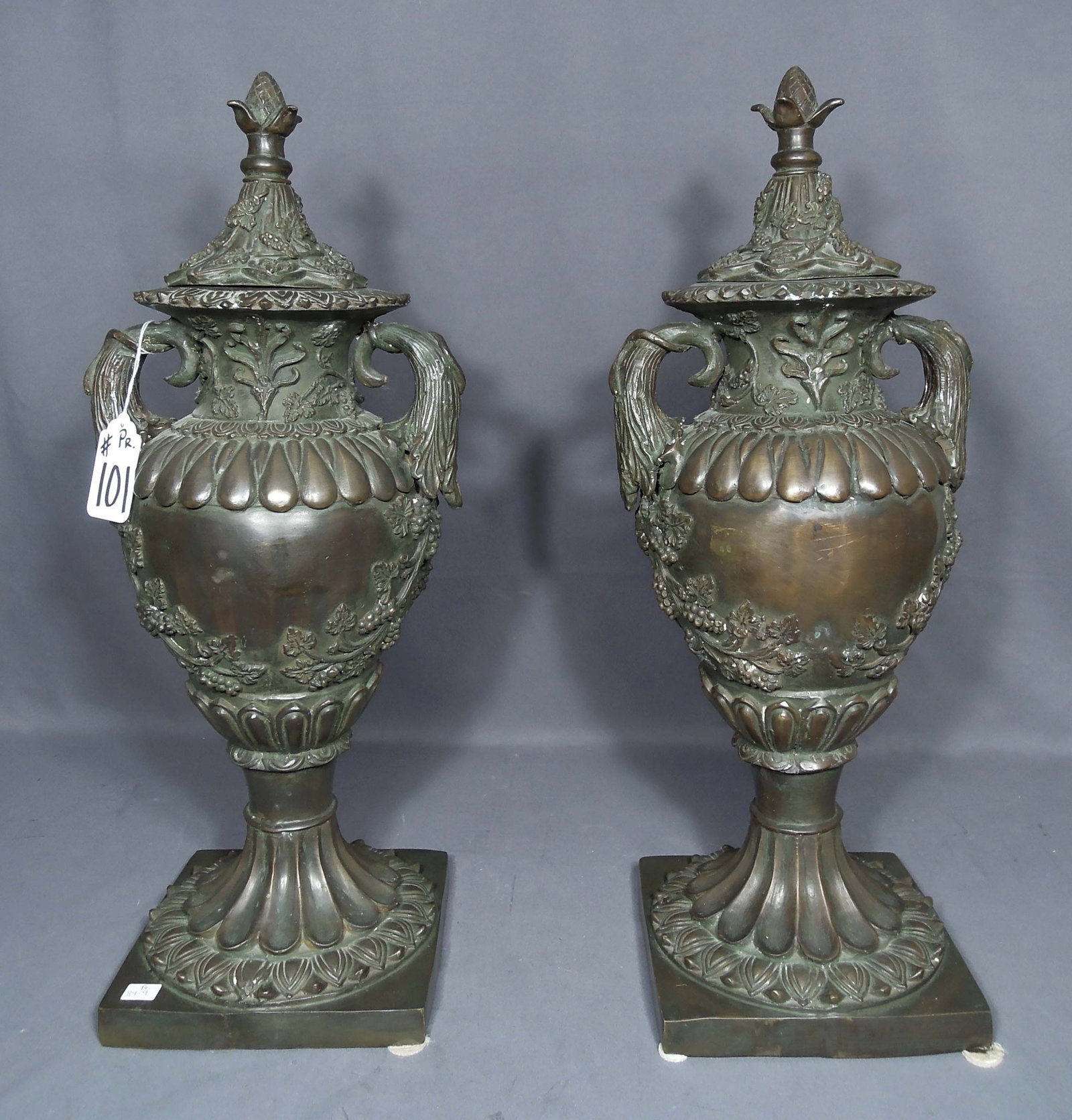 PAIR VINTAGE BRONZE URNS WITH LIDS: Grape motif. Two handles. 25" high, 10" wide, 8 1/2" deep.