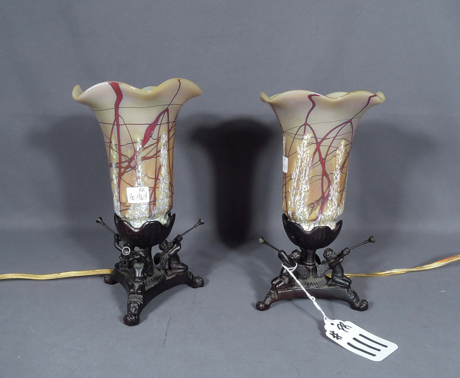 PAIR VERY RARE CARL RADKE BRONZE AND ART GLASS SMALL SCALE LAMPS: A vintage Art Nouveau style base with cherubs blowing horns. Each base supports an art glass tulip shade signed Carl Radke. Excellent condition. Overall 9" high, 5" dia.