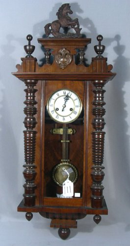 ANTIQUE GUSTAV BECKER WALL CLOCK: A finely carved wooden clock with Roman numeral dial and horse motif finial. Inside plaque: Gloria. 39" high, 14 1/2" wide.