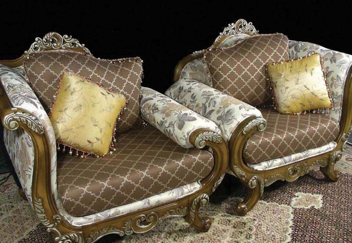 PAIR UNUSUAL LARGE CARVED WOOD AND UPHOLSTERED CHAIRS: A daybed style corner chair with ornate carvings on legs and rails. Curved arms. Brown, gold and beige floral motif upholstery. Complete with four over stuffed pillows.