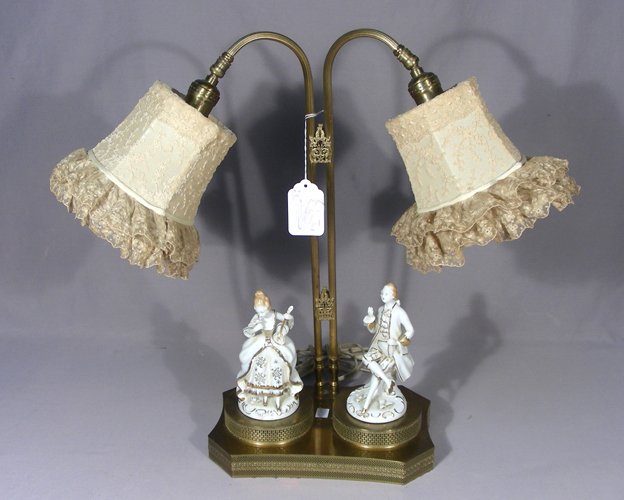 ANTIQUE BRASS AND PORCELAIN TWO LIGHT TABLE LAMP: A scalloped brass open work base with two porcelian figures and a two armed light with antique lace shades. 20" high, 22" wide.