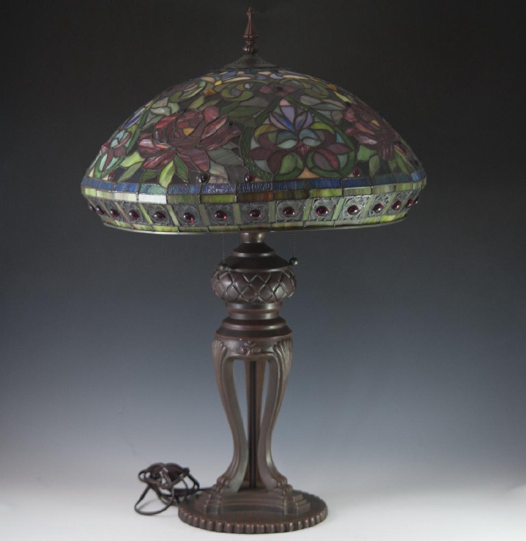 Tiffany Style Lamp: DESCRIPTION: A reproduction, Tiffany style lamp. Features a composite foundation made to look as a rusted bronze. Features three lion paw motif legs along the stem, standing atop a ridged, and beveled