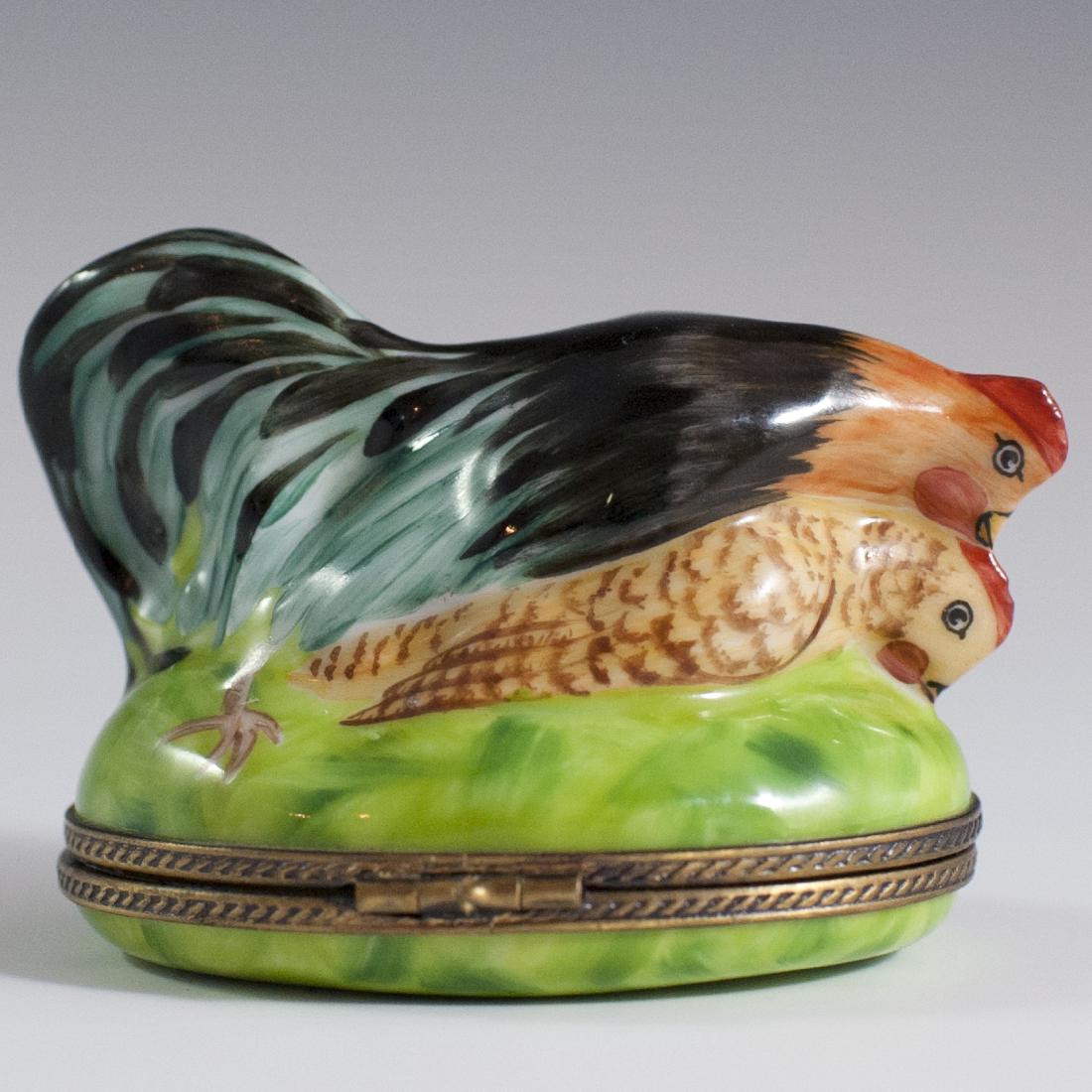 Limoges Porcelain Trinket Box: DESCRIPTION: A Limoges porcelain trinket box Featuring two naughty roosters along the lid. Fitted with with a brass lined clasp in the motif of a cockerel. Opens to reveal a white interior and is mark