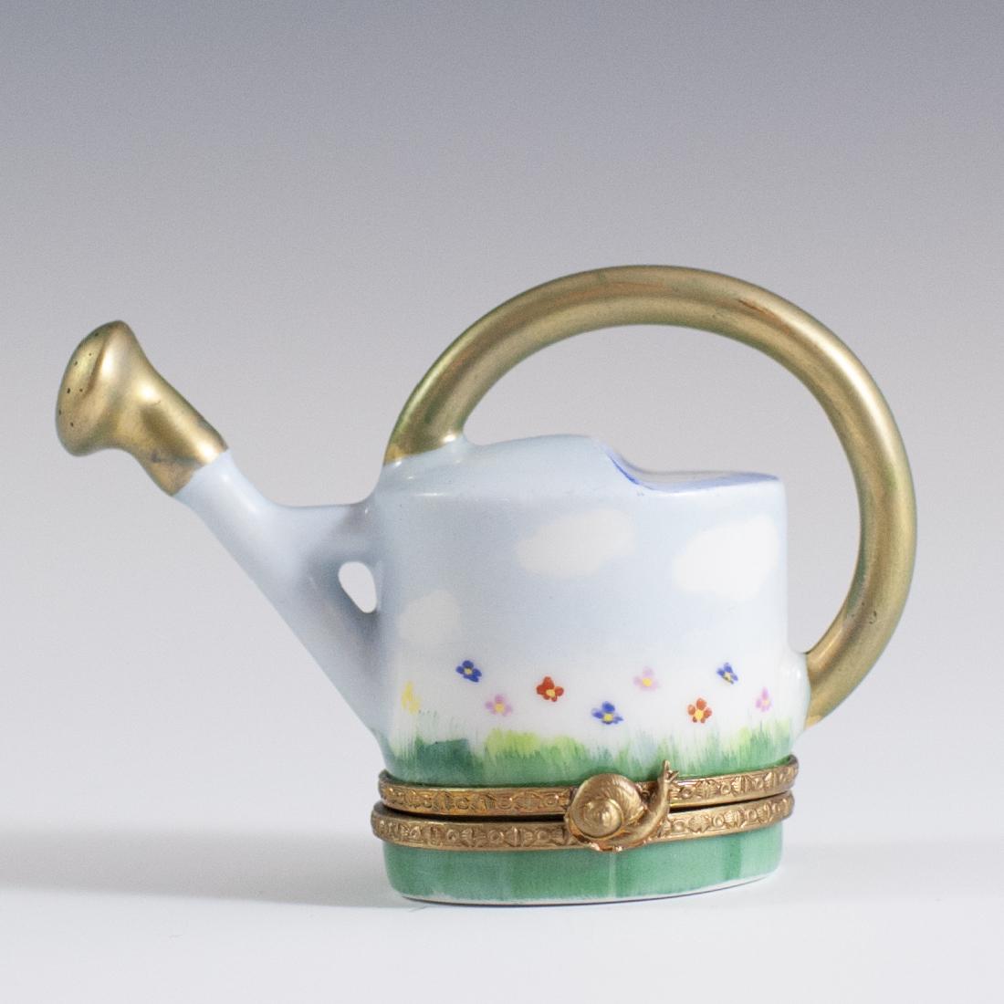 Limoges Porcelain Trinket Box: DESCRIPTION: A Limoges porcelain trinket box in the motif of a watering can embellished with celeste blue sky and floral motifs. Finished with gilded trims along the handle and spout along with a gilt