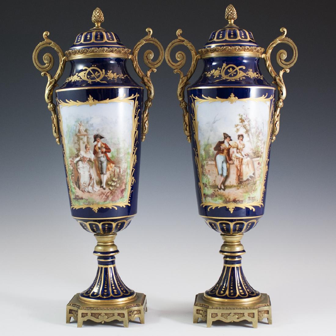 Bernardaud Limoges Sevres Stamped Porcelain Urns: DESCRIPTION: A Bernardaud & Co. Limoges pair of porcelain urns. Features mounted dore bronze applications along the base, stem, and scrolled rococo acanthus leaf motif handles. Further garnished with