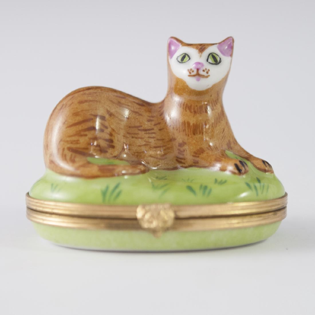 Tiffany & Co. Limoges Porcelain Pill Box: DESCRIPTION: A Tiffany & Co. Limoges porcelain pill box. Features a kitten lying on the ground, atop the oval, hinged lid garnished by a gilt clasp with a tiger head clasp. Marked along the underside: