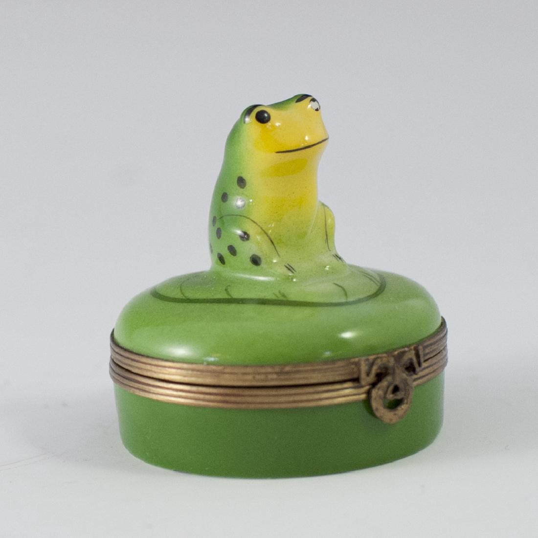 Castel Limoges Porcelain Pill Box: DESCRIPTION: A Castel Limoges porcelain pill box. Features a rotund form and a toad figurine along the lid, atop a lily pad. Finished with a gilt metal clasp and a wreath motif clasp. Marked:"Limoges 