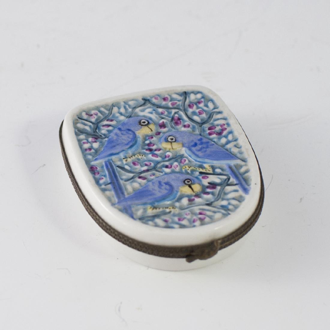 Limoges Porcelain Pill Box: DESCRIPTION: A Limoges porcelain pill box. Features an embossed decoration along the lid of parrots atop tree branches. Finished with a metal lining and a bird motif clasp. Marked:"Peint Main Limoges 