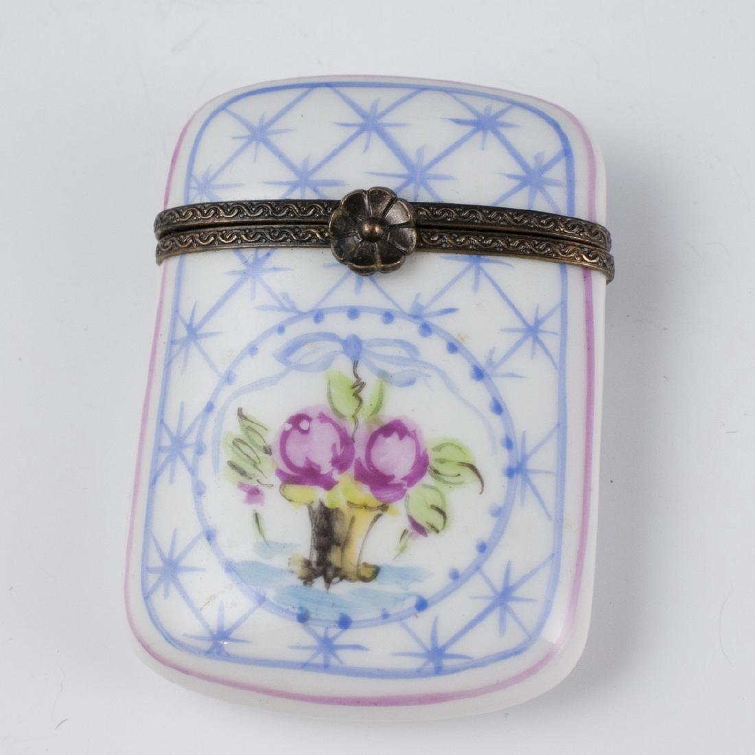 Limoges Porcelain Pill Box: DESCRIPTION: A Limoges porcelain pill box. Features a rectangular form with rounded edges garnished with a center motif of roses in a vase. Finished with a metal lining and a rose motif clasp. Marked: