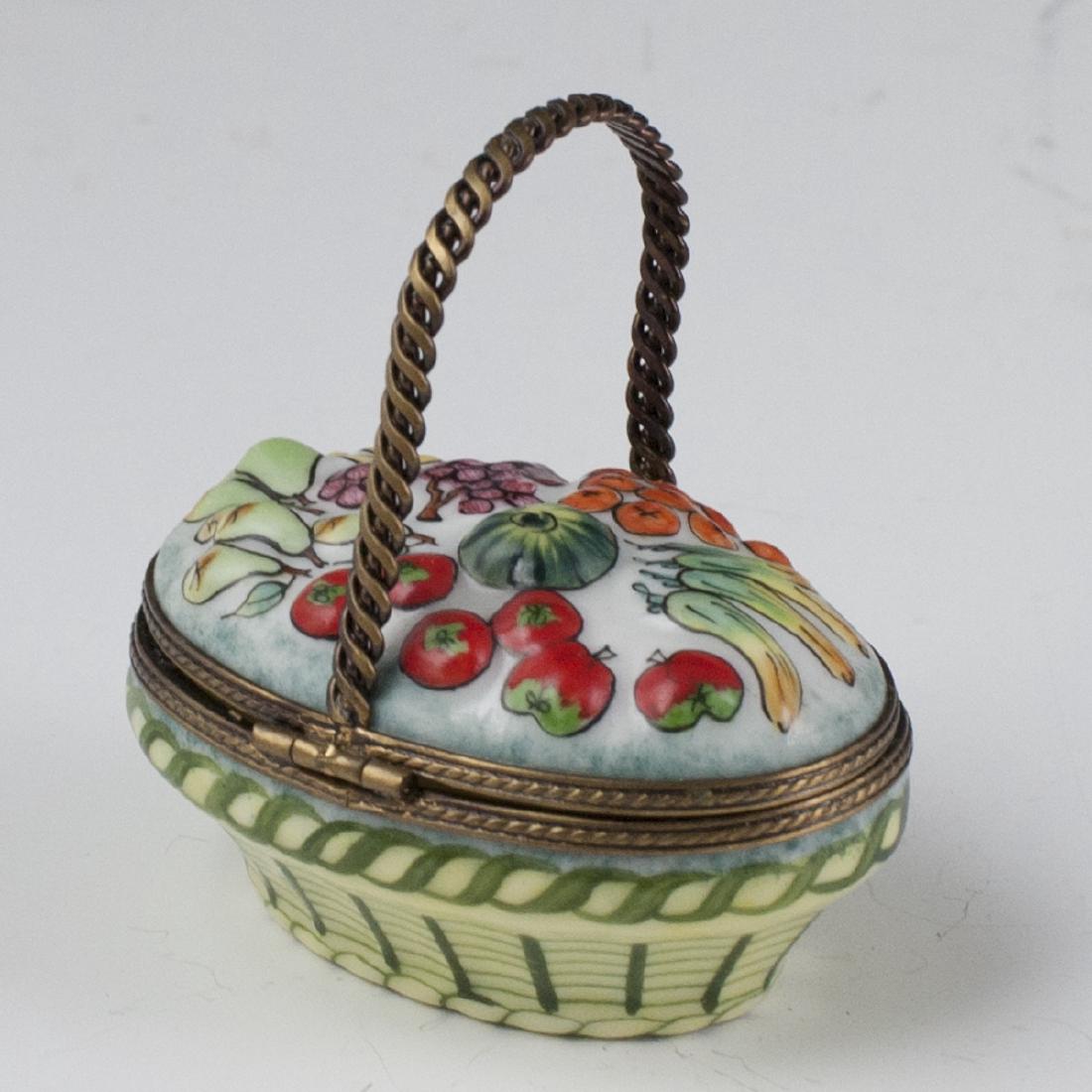 Limoges Porcelain Pill Box: DESCRIPTION: A Limoges porcelain pill box in the motif of a basket, garnished with an array of embossed produce along the lid. Finished with a gilt metal handle, lining, and grape cluster motif clasp.