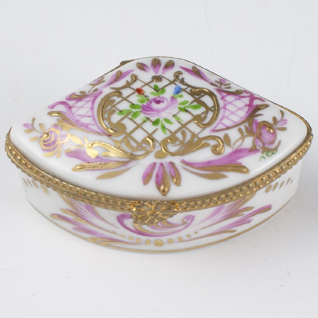 Limoges Porcelain Pill Box: DESCRIPTION: A Limoges porcelain pill box. Features an overall scrolled rococo floral motif with pink hued accents and gilded enameled detailing. Finished with a gilt metal lining and a floral motif c