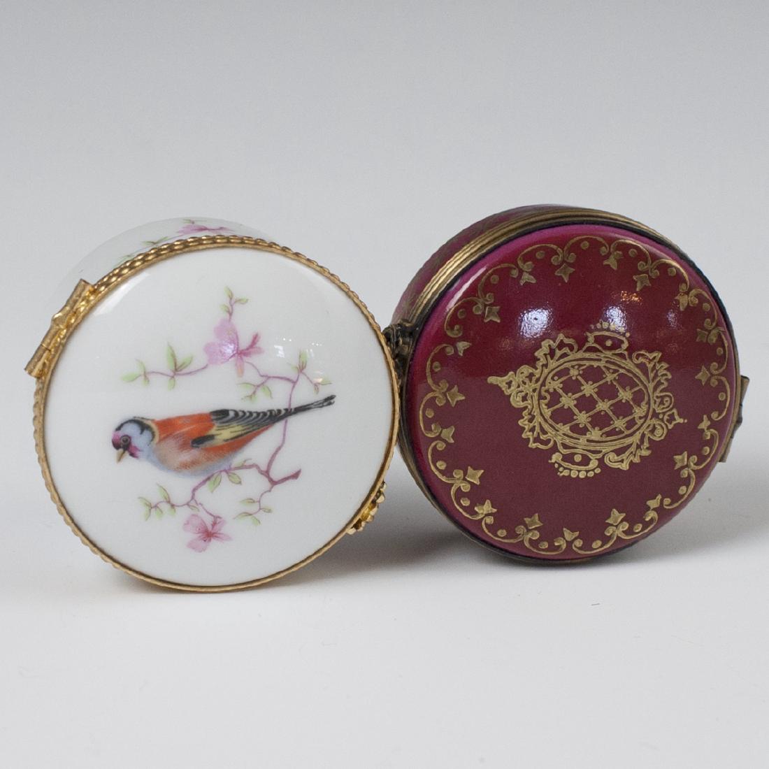 Limoges Porcelain Pill Boxes: DESCRIPTION: A pair of porcelain pill boxes. The first is embellished along the lid with a scene of a bird perched atop a tree branch. Finished with a gilt metal lining and a floral motif clasp. Marke