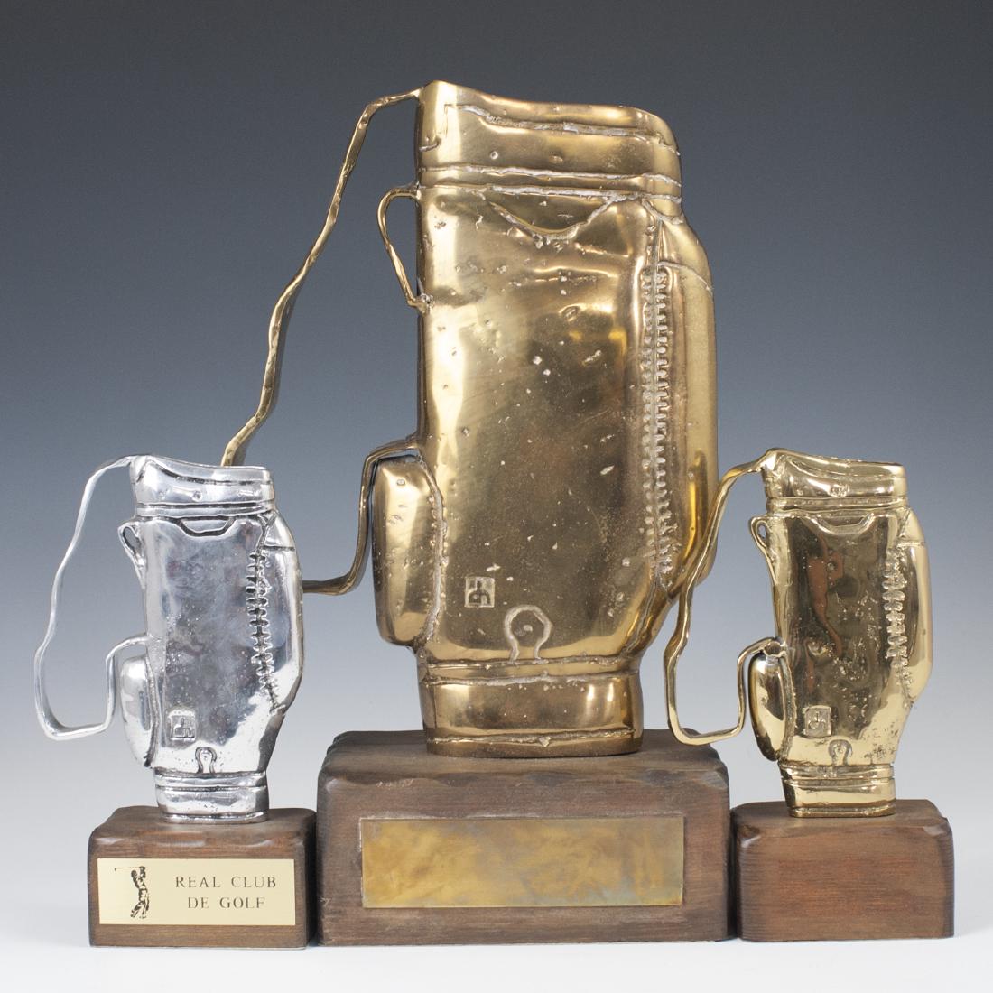 David Marshall Gold Bag Trophies: DESCRIPTION: A set of three David Marshall trophies in the motif of golf bags. Composed of one aluminum trophy, and two brass trophies, one smaller, one larger. All are fitted to wooden bases. The alu