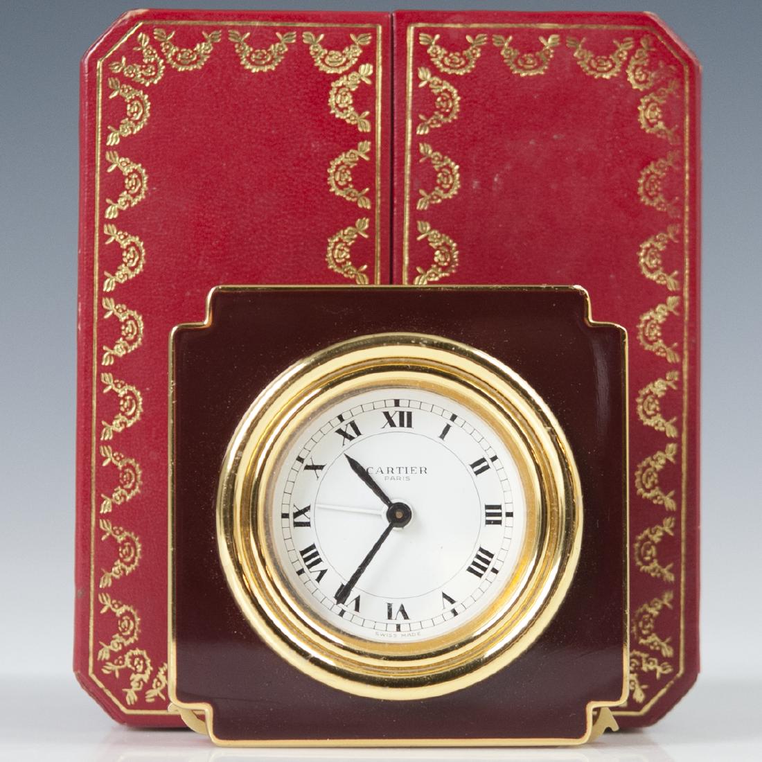 Cartier "Vendome" Travel Clock: DESCRIPTION: A Cartier "Vendome" travel clock .Features a gold plated foundation, garnished with a burgundy hued enamel enveloping the center face with Roman numeral dials. Finished with sapphire cabo