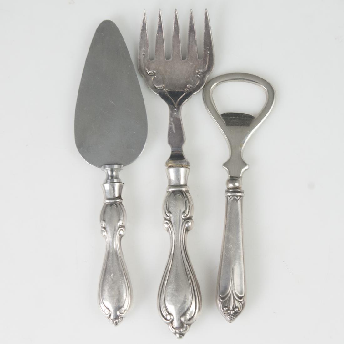Sterling Flatware Set: DESCRIPTION: A flatware set composed of a bottle opener, a cheese knife, and a fork. Embellished with stainless blade and sterling handles with Rococo designs. CIRCA: Early-Mid 20th Ct. DIMENSIONS: (f