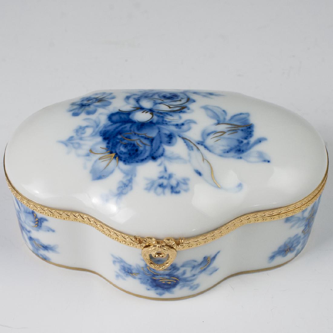 MNP Limoges Porcelain Dresser Box: DESCRIPTION: An MNP Limoges porcelain dresser box. Features a waved design, garnished by blue rose motifs lined by gilded accents. Finished with a gilt metal lining and a wreath motif clasp. Marked al