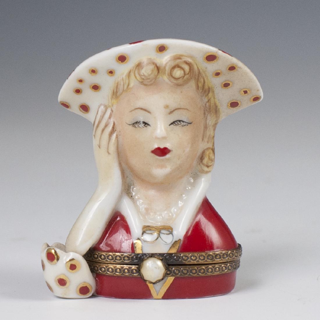 Limoges Porcelain Pill Box: DESCRIPTION: A Limoges porcelain pill box in the motif of a woman wearing a dotted hat, with her head resting on her hand with an aperture along her hat to be used as a lipstick holder. Finished with 