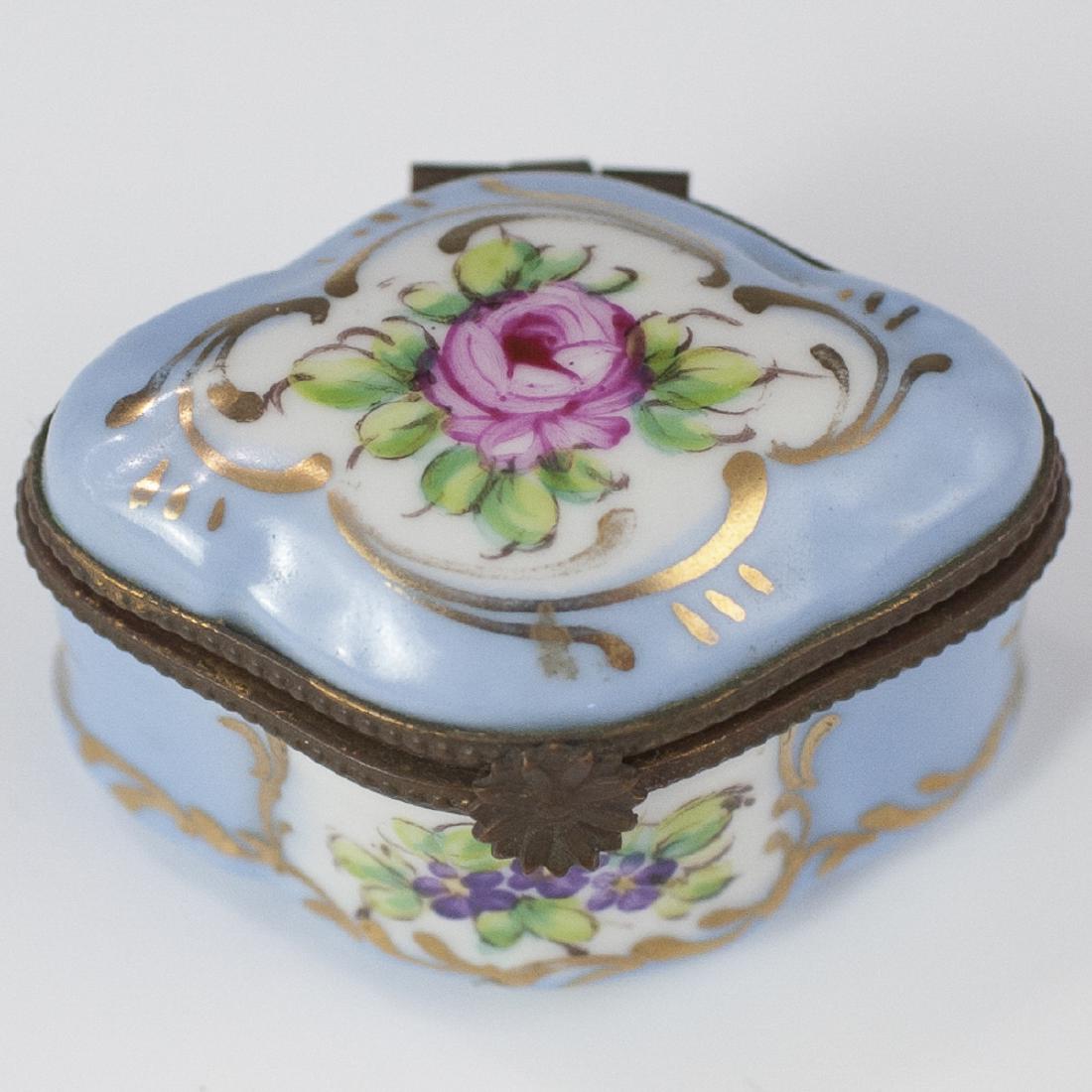 Limoges Porcelain Pill Box: DESCRIPTION: A Limoges porcelain pill box. Features floral motif scenes enveloped by a celeste blue base hue, embellished with gilded trims. Finished with a gilt metal lining and a floral motif clasp.