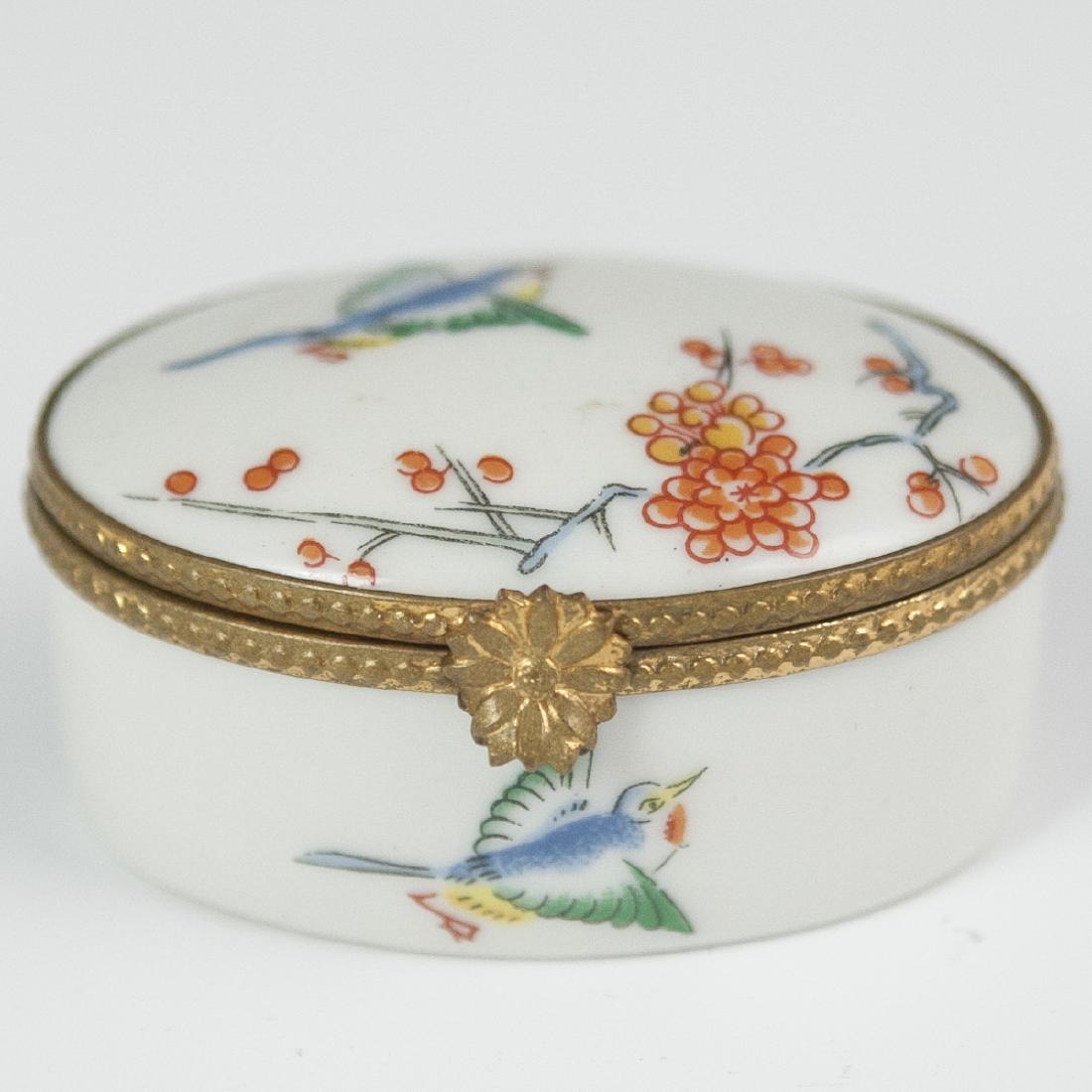 Castel Limoges Porcelain Pill Box: DESCRIPTION: A Castel Limoges porcelain pill box. Features an oval form and garnished with Chinoiserie style soaring bird and blossom motifs. Finished with a gilt metal lining and floral motif clasp. 
