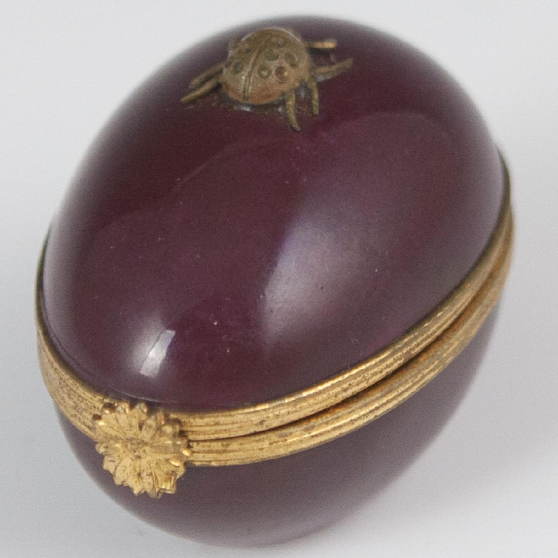 Limoges Porcelain Pill Box: DESCRIPTION: A Limoges porcelain pill box. Features an ovoid form, embellished with a burgundy base hue, and centered by a lady bug along the lid. Finished with a gilt metal rosette motif clasp. Marke