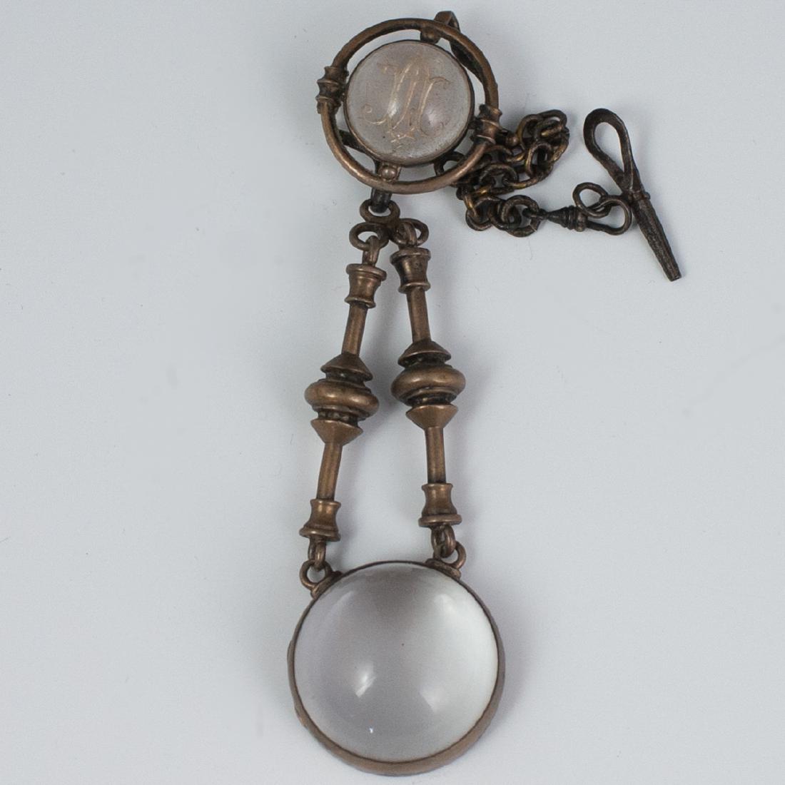 Victorian Crystal Intaglio Fob: DESCRIPTION: A Victorian fob designed with a silver toned metal chain convening at a top crystal intaglio with a monogram. Below the intaglio are two spindled prongs which convene at the bubble magnif