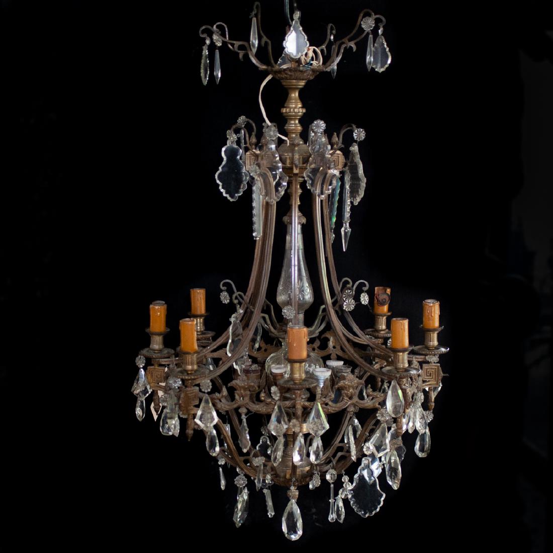 Bronze & Crystal Chandelier: DESCRIPTION: A bronze and crystal chandelier. Featues an overall bronze foundation adorned with hanging crystal prisms and rosettes throughout. Further designed with a cut crystal stem, with 8 interio