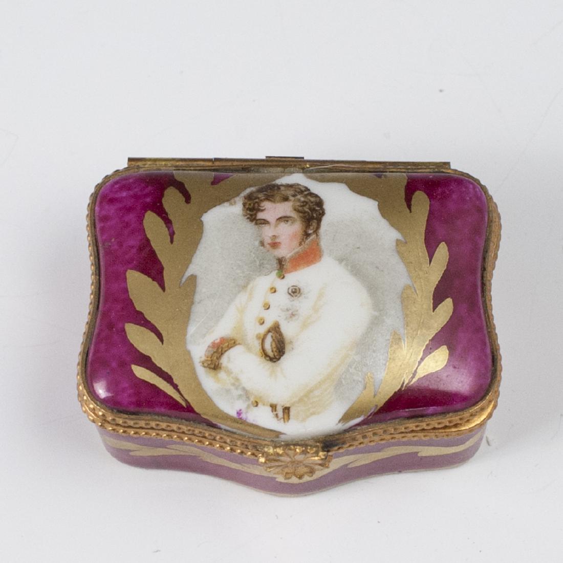 Limoges Porcelain Trinket Box: DESCRIPTION: A Limoges porcelain trinket box. Features a maroon red base hue, centered by a portrait of an aristocratic man enveloped by gilded accents. Finished with a gilt metal lining with a floral