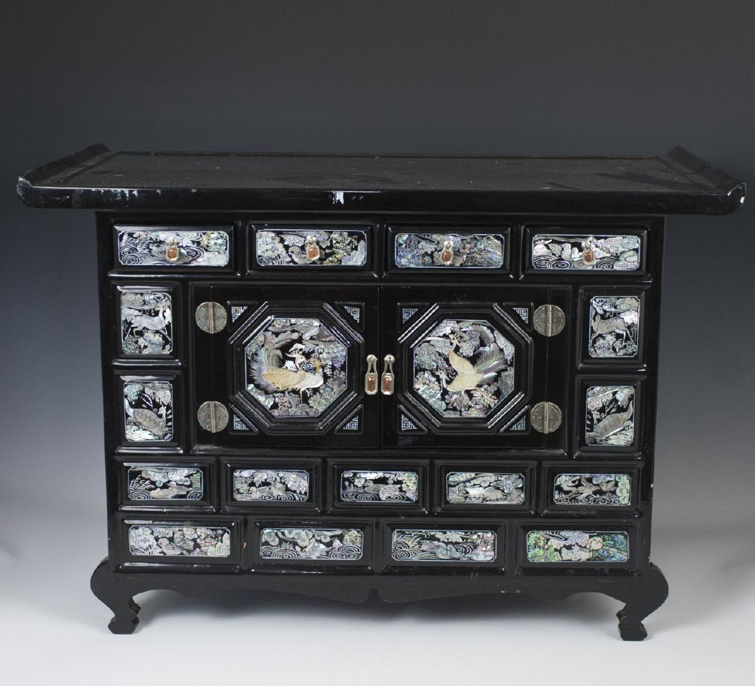 VintageLacquered Mother of Pearl Cabinet: DESCRIPTION: A vintage Korean, lacquered mother of pearl cabinet. Features an overall, black toned, lacquered foundation with a flattened surface along the top and arching feet intersected by waved sk
