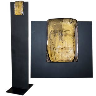 Luigi Benzoni (Italian b.1956): DESCRIPTION: A murano glass and iron sculpture by Luigi Benzoni. Features a murano glass slab with an abstract visage, enveloped with gold leaf. Slides into the cast iron stand with the appearance as