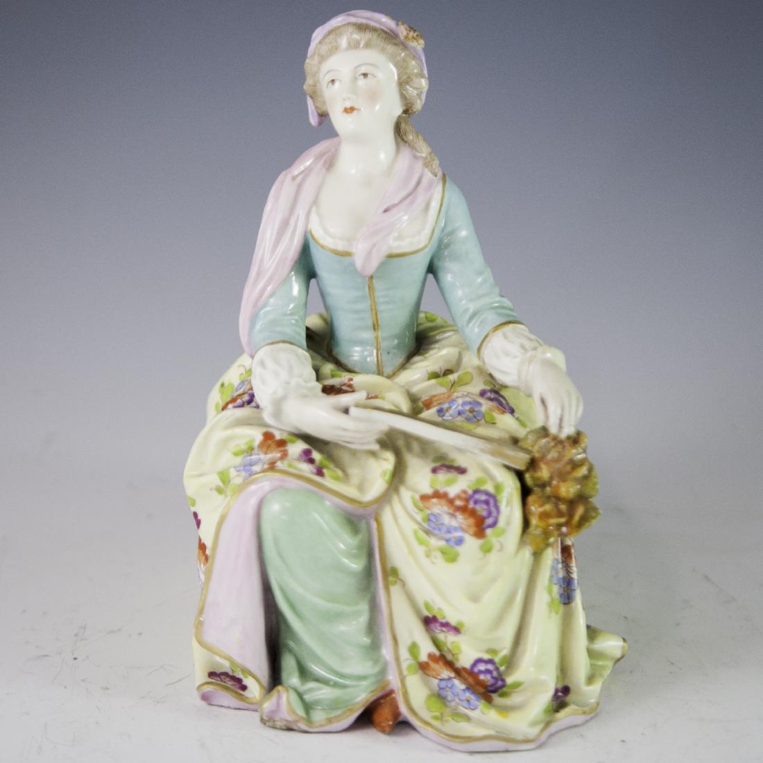 Antique Kalk German Porcelain Figurine: DESCRIPTION: An antique Kalk of Eisenberg German porcelain figurine. Features an Edwardian era woman wearing long flowing floral motif garments and elaborate head dress as she sits on a boulder holdin