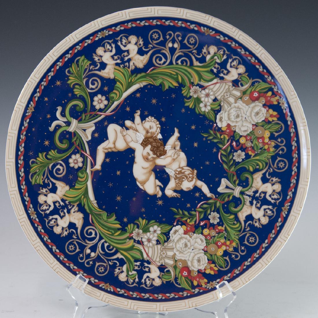 Rosenthal "Christmas With Versace" Porcelain Charger: DESCRIPTION: A Rosenthal "Christmas With Versace" porcelain charger. Features three soaring cherubs enveloped by stars and winding, scrolled foliage convening at fruit filled cornucopias intersected b
