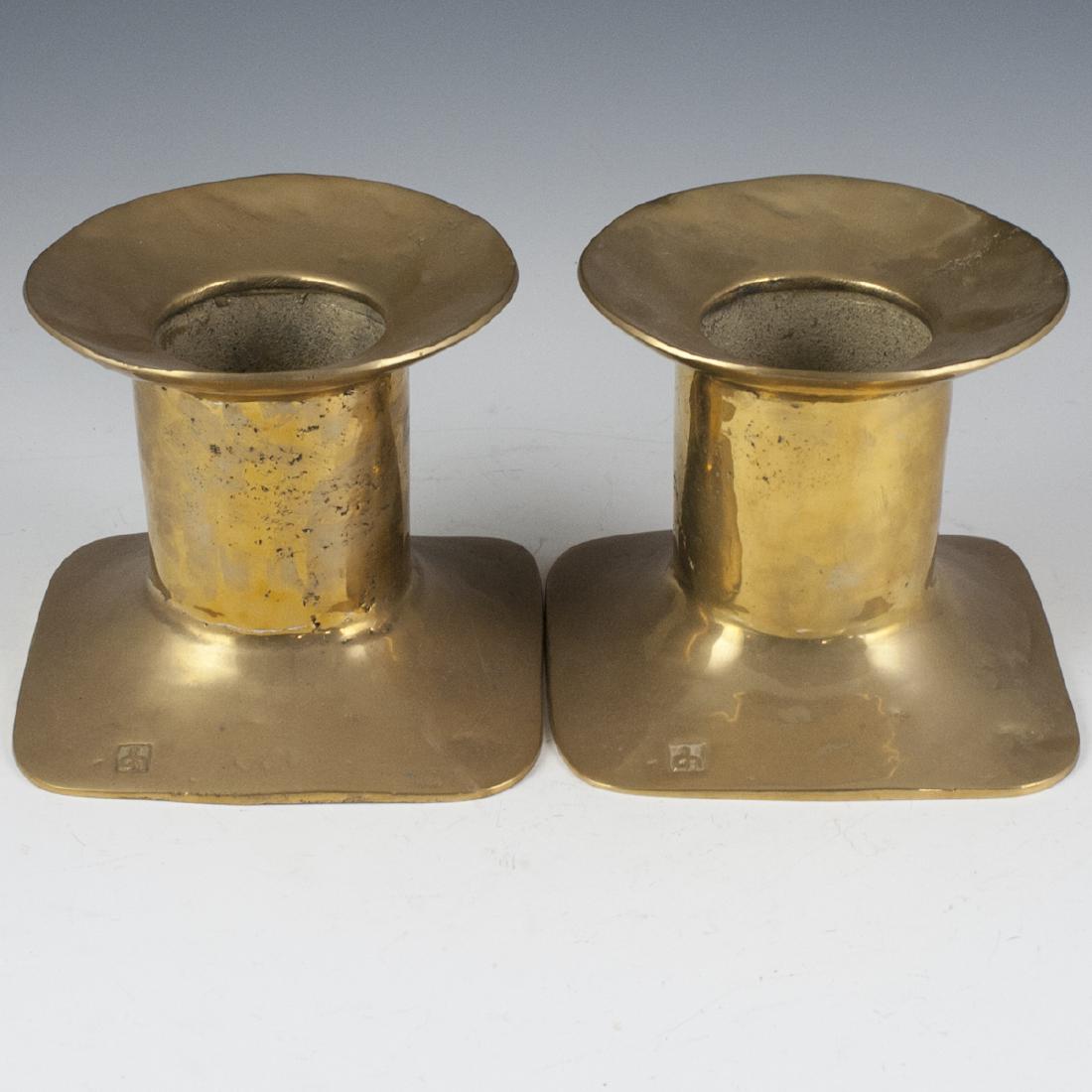 David Marshall Brass Candlesticks: DESCRIPTION: A pair of David Marshall brass candlesticks, for large candles. Composed of an overall brass foundation with a squared base, fluted stem and arching rim. Marked with David Marshall marks.