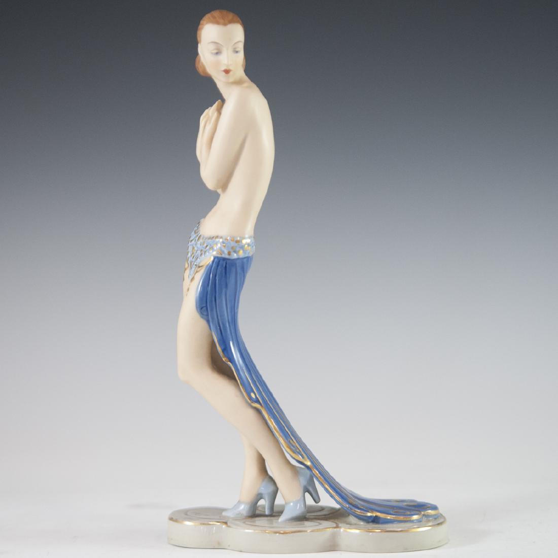 Art Deco Royal Dux Bisque Figurine: DESCRIPTION: An Art Deco, bisque porcelain figurine of a partially nude female dancer wearing a gilded peacock tail dress with gilded accents. Finished with a glossed glaze along the dress and base. M