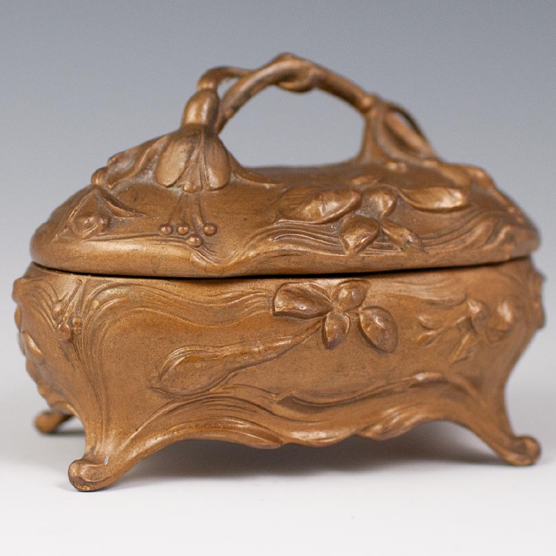Jennings Brothers Art Nouveau Jewelry Box: DESCRIPTION: A brass art nouveau jewelry box by Jennings Brothers. Features a round footed design, with floral motif throughout. Marked on the bottom "336" and "JB" CIRCA: 20th ORIGIN: USA DIMENSIONS: