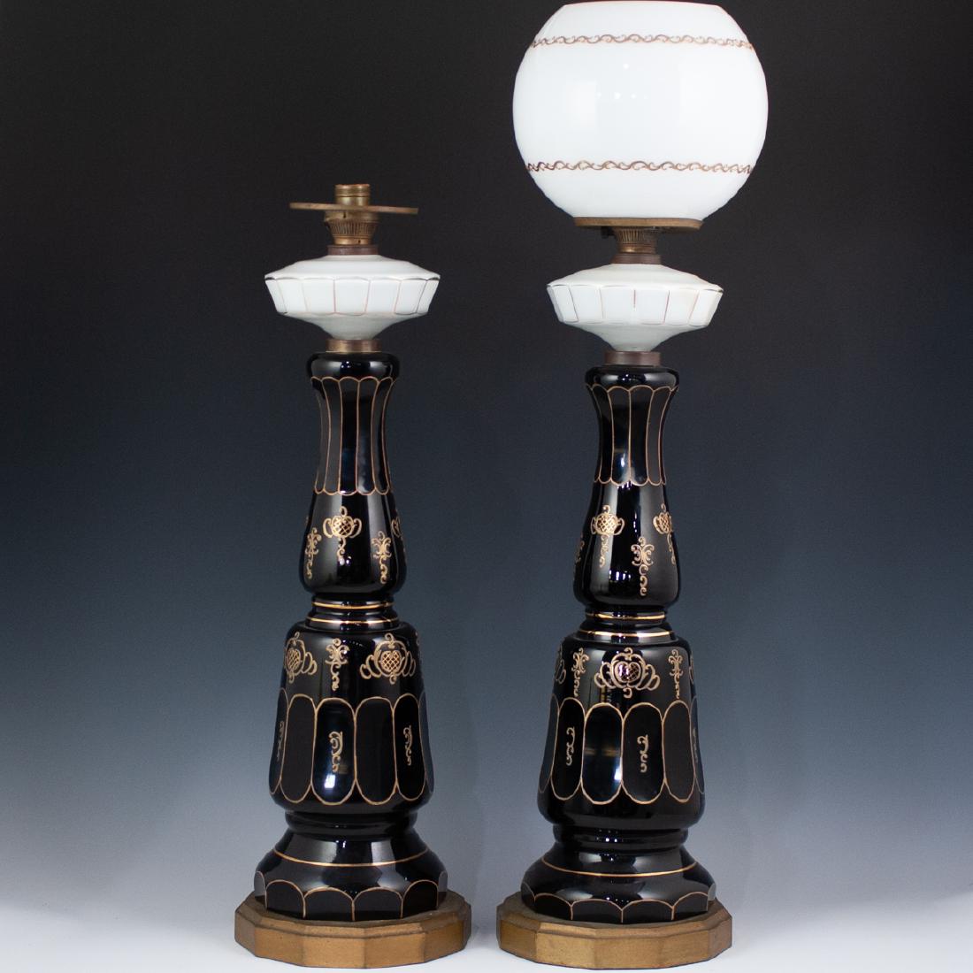Pair Of Bohemian Monumental Glass Lamps: DESCRIPTION: Pair of Bohemian converted oil, enameled glass lamps feature in a Noir base hue, embellished with hand painted gilded trims and baroque motifs. Each lamp supports an opaline glass oil tan