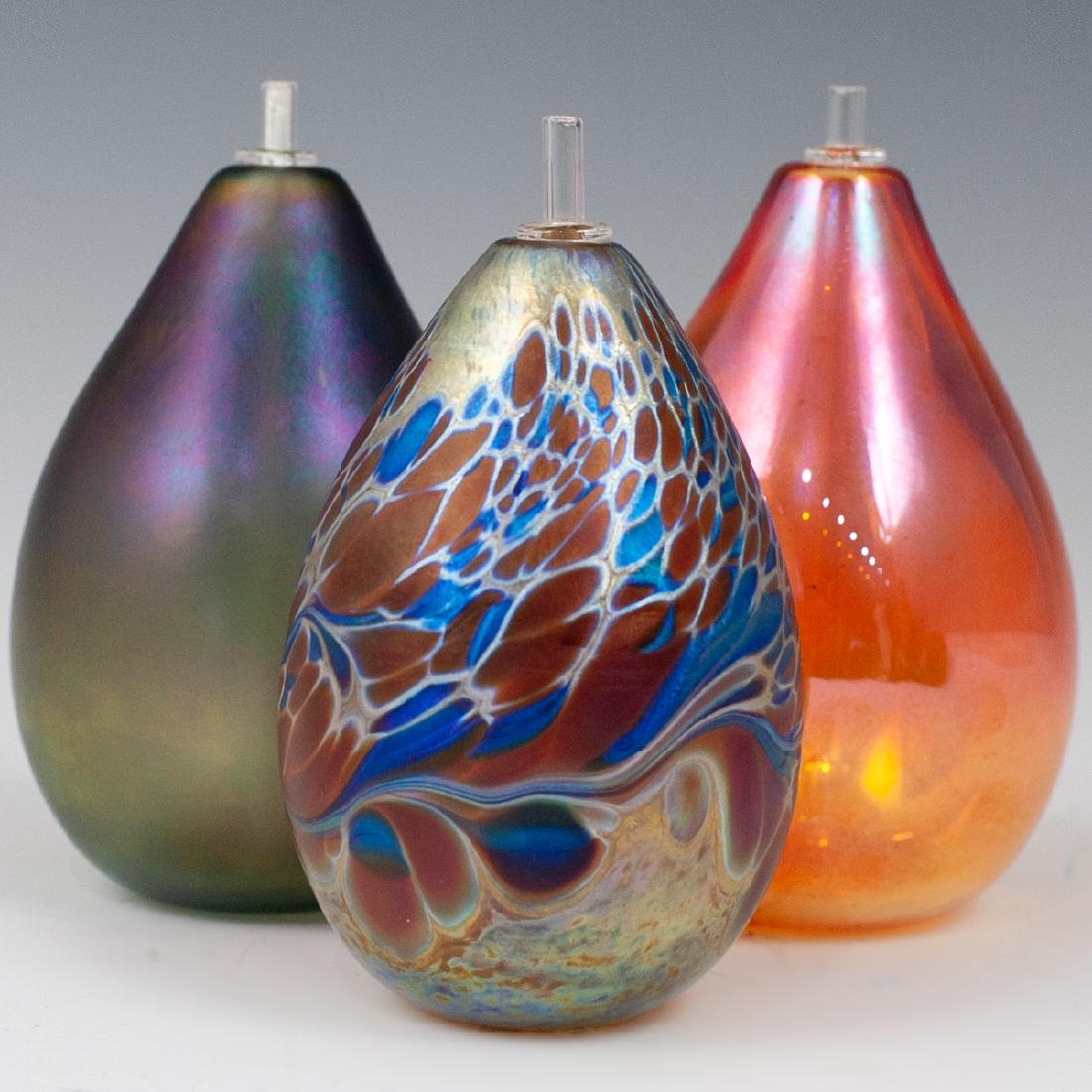 (3 Pc) Brian Maytum Art Glass Oil Lamps: DESCRIPTION: A lot of three pear shaped art glass oil lamps. Each featuring a unique iridescent design including a perfume dabber, signed along the underside "Brian Maytum Studios 1985". CIRCA: Late 2