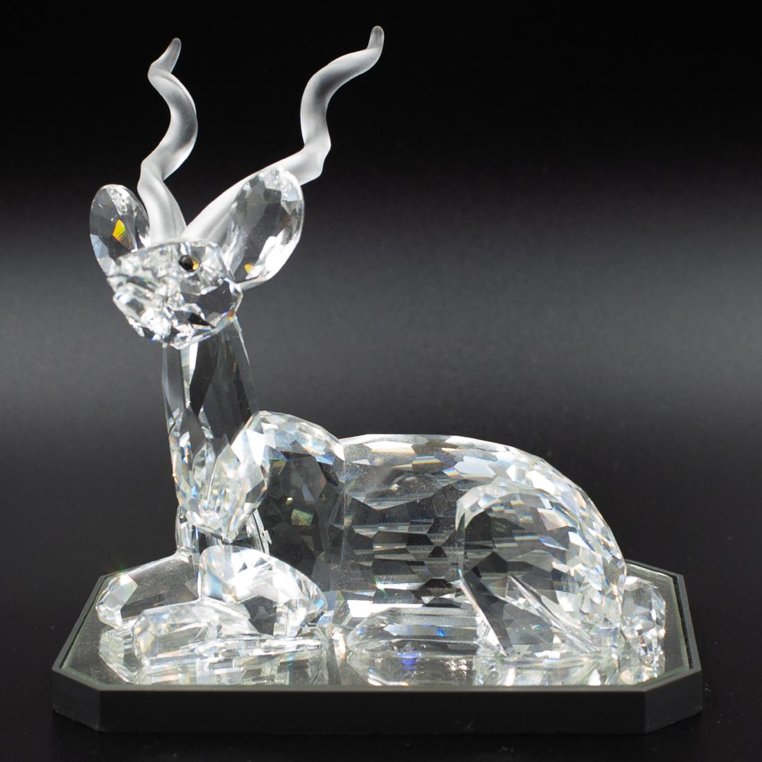 Swarovski Crystal Antelope Figurine: DESCRIPTION: A Swarovski crystal figurine of a reposed antelope. Features an overall faceted crystal body with frosted crystal antlers. Marked with a Swarovski back stamp. Includes a mirror base. CIRC