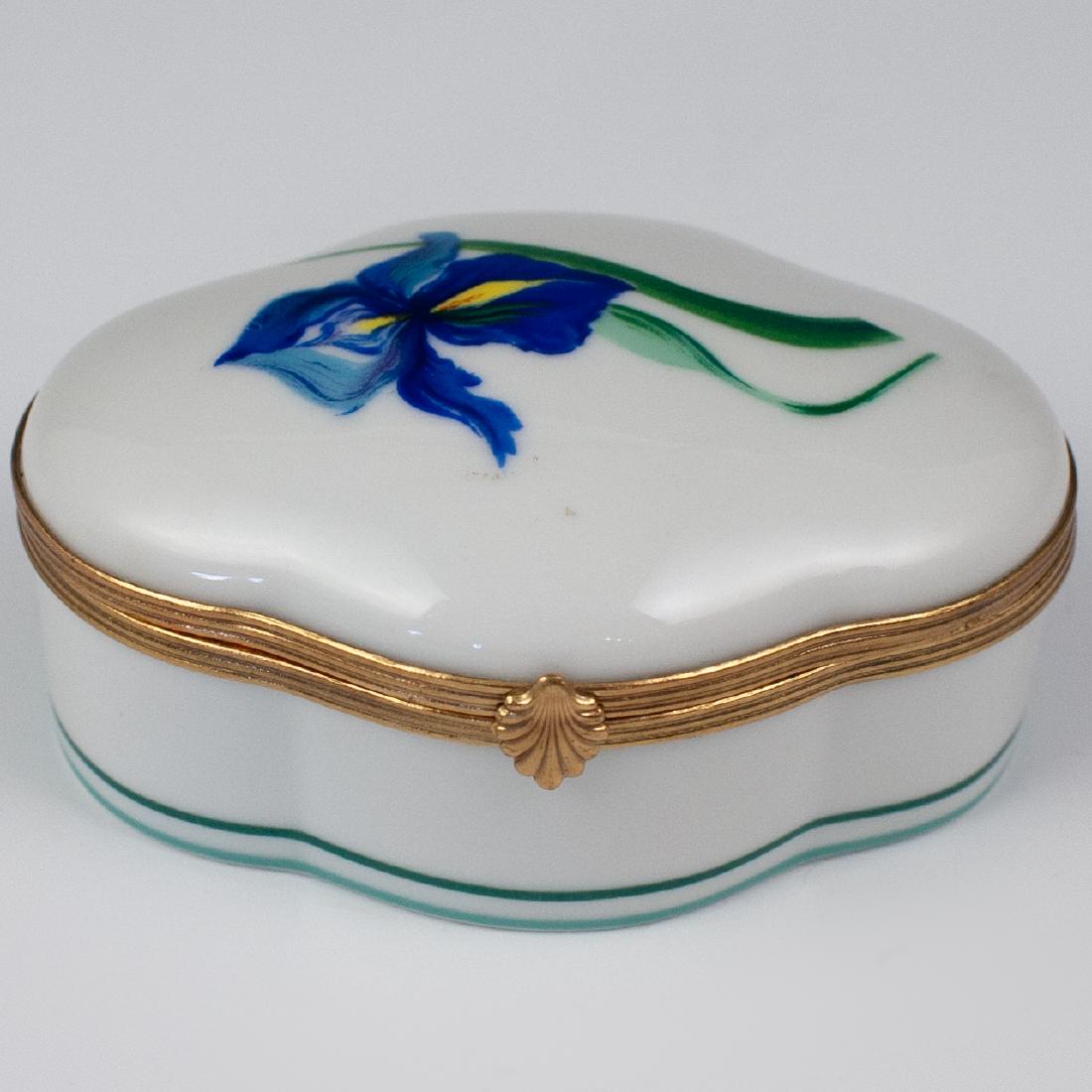 Limoges Porcelain Orchid Box: DESCRIPTION: A Limoges porcelain box features in an overall oval form, handpainted along the rim with a blue orchid motif and double lines encompassing the bottom. Marked along the underside "A. Rayna