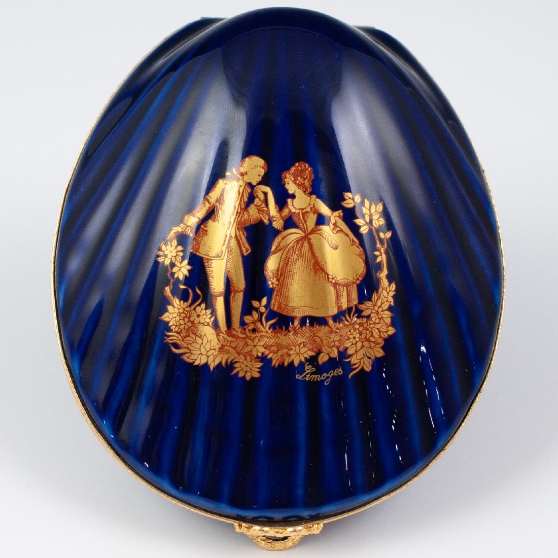 Limoges Porcelain Cobalt Trincket Box: DESCRIPTION: A Limoges porcelain trincket box features in a clam shape, painted in a cobalt blue ground color and embellished along the rim with courting couples in gilded hues. The sides are fitted w