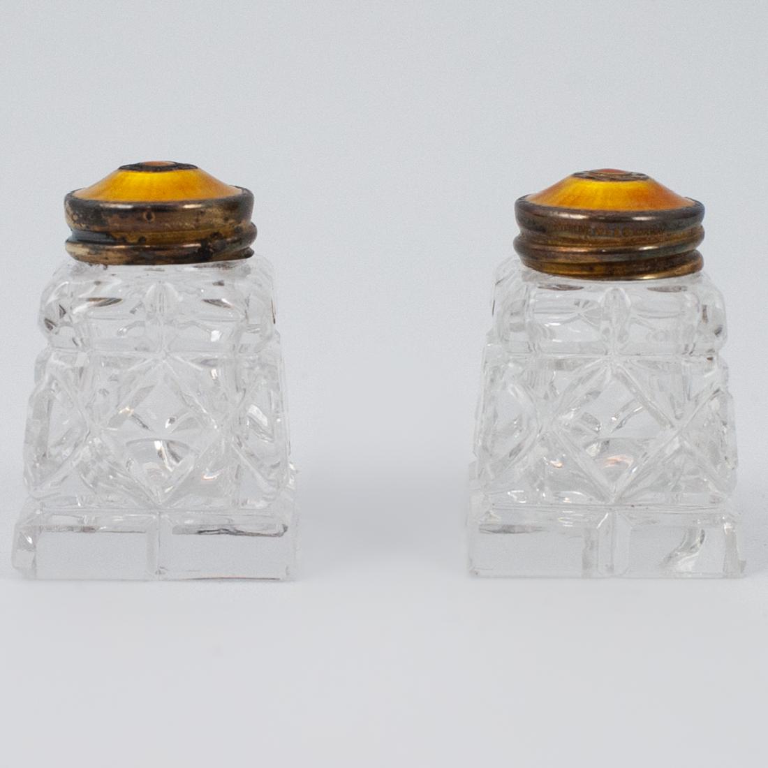 Pair of Norwegian Sterling and Enamel Shakers: DESCRIPTION: A Pair of Norwegian sterling silver and enamel cut glass salt and peppers. With gold enamel and guilloche colored twist-on tops over cut crystal vessels. Hallmarked on the rim: "Sterling 