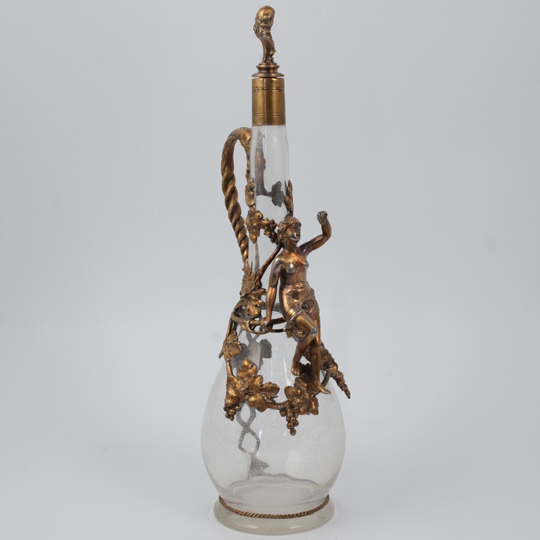 Silver and Glass Figural Decanter: DESCRIPTION: The glass decanter features a bulbous bottom tapering to a long neck. Wrapped along the center are figural silver plate overlay depicting a nude maiden and various berry and leaf decorati