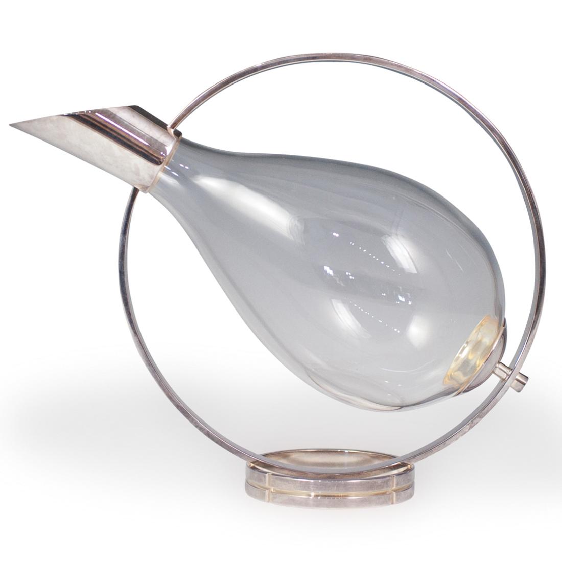 Christofle "Fidelio" Silver Plated and Glass Wine: DESCRIPTION: A Christofle "Fidelio" silver-plated and glass wine decanter. Features a simple orbital design with a bulb shaped glass wine holder. Marked: "Christofle" on the base. CIRCA: 20th Century