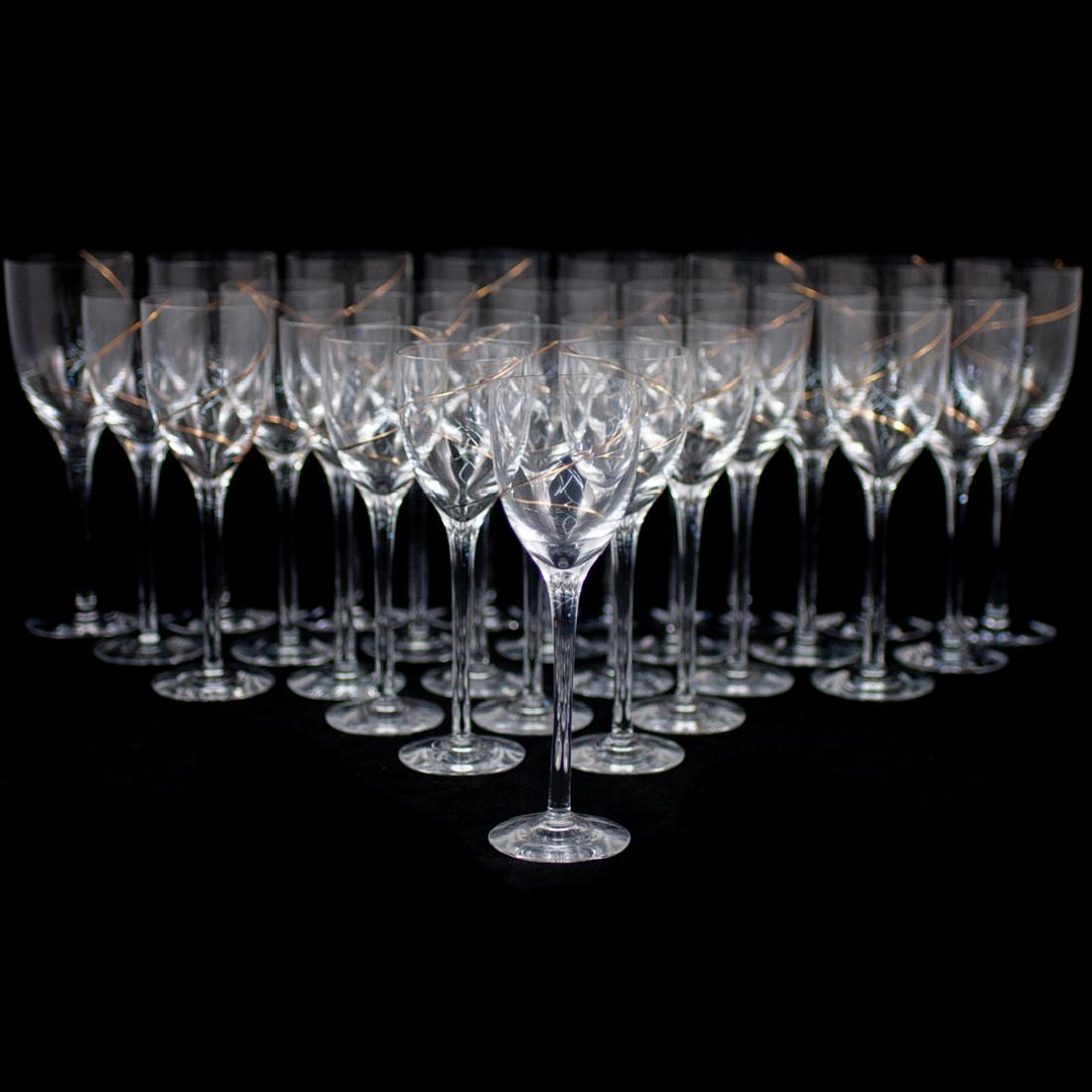 (27 Pc) Kosta Boda Line Gold Crystal Wine Glass Set: DESCRIPTION: A 27 piece Kosta Boda crystal wine glass set. Features glasses for red and white wine with additional liquor glasses. Each cup is embellished along the body with a swirled gilt line patte