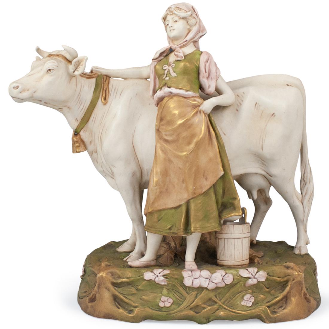Royal Dux Porcelain Milkmaid and Cow: DESCRIPTION: A 'Royal Dux' hand-painted porcelain figurine. Features a milkmaid standing in front of a cow with her right hand on a tethered rope around the cow's neck, executed in a glaze porcelain f