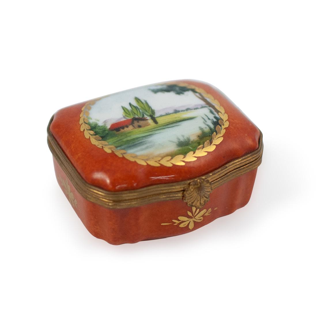 Limoges Porcelain Countryside Trinket Box: DESCRIPTION: A Limoges porcelain trinket box embellished with countryside scenes along the rim in an overall rusted orange ground color, completed with gilded brass lining and a clam motif clasp. Mark