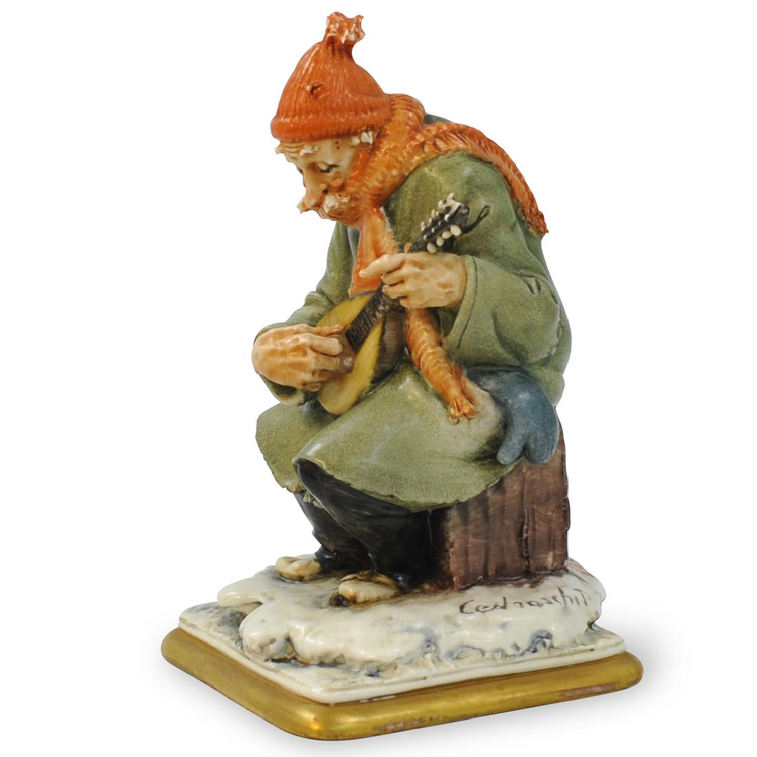 Cedraschi Capodimonte Figurine: DESCRIPTION: A 'Creazioni Cedraschi' Capodimonte figure. The figurine depicts a seated older gentleman playing a stringed instrument wearing a coat, scarf and hat. Made by Milanese artist Piergianni C