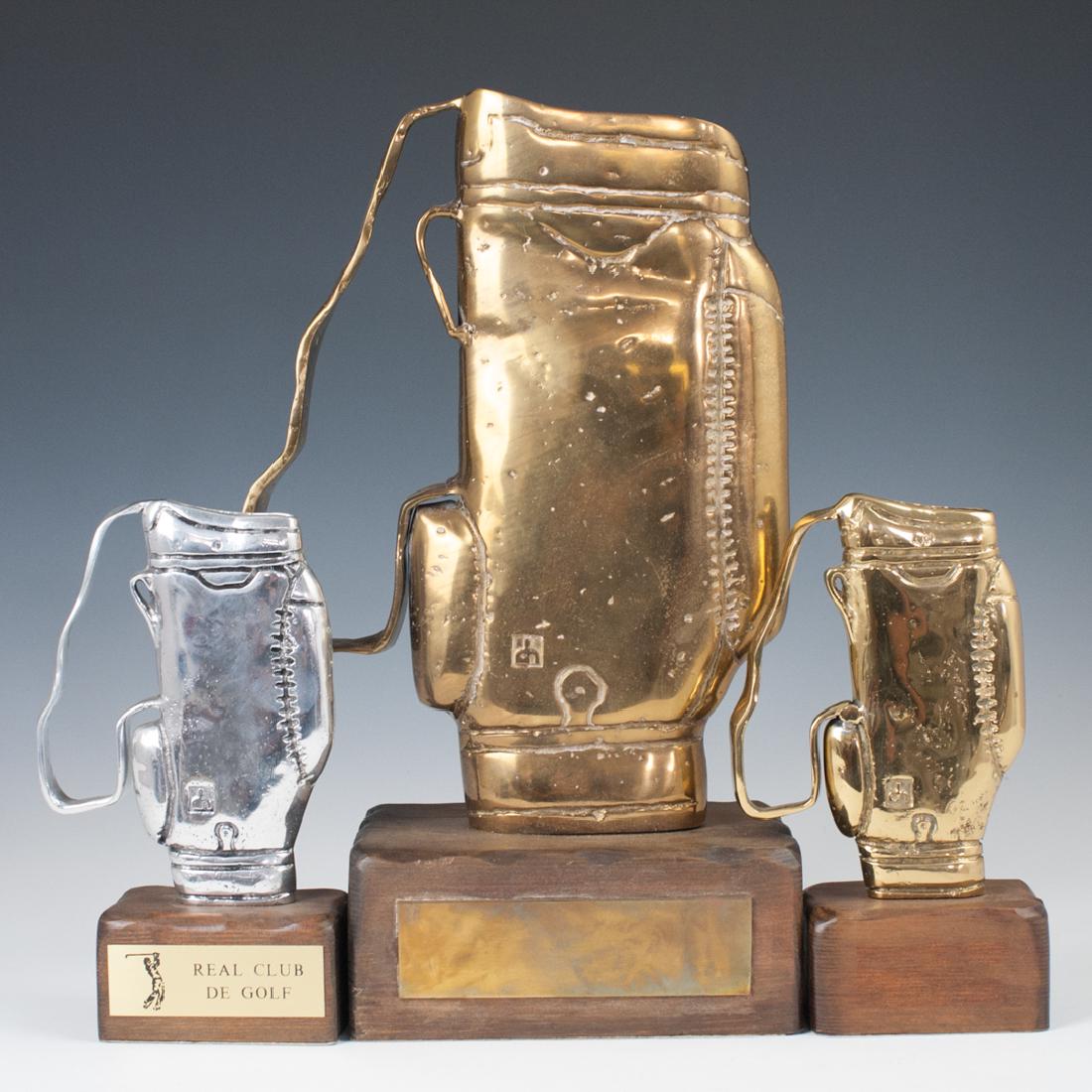 David Marshall Gold Bag Trophies: DESCRIPTION: A set of three David Marshall trophies in the motif of golf bags. Composed of one aluminum trophy, and two brass trophies, one smaller, one larger. All are fitted to wooden bases. The alu
