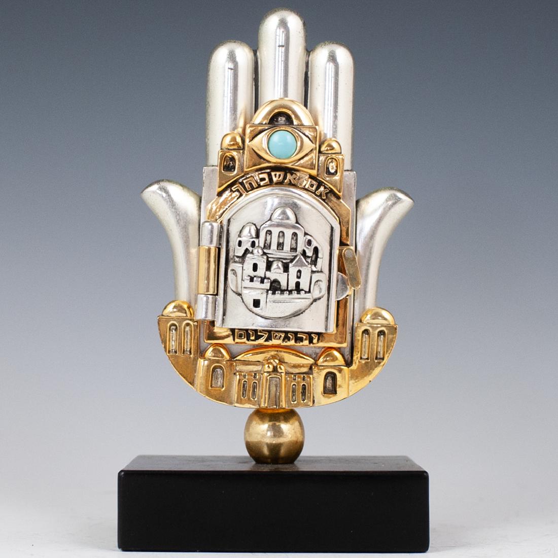 Frank Meisler Style Sterling Judaic Ornament: DESCRIPTION: A Frank Meisler style, sterling Judaica ornament in the motif of a Hamsa hand centered by a swiveling door that opens to reveal a prayer in Hebrew, topped by a turquoise cabochon. Finishe